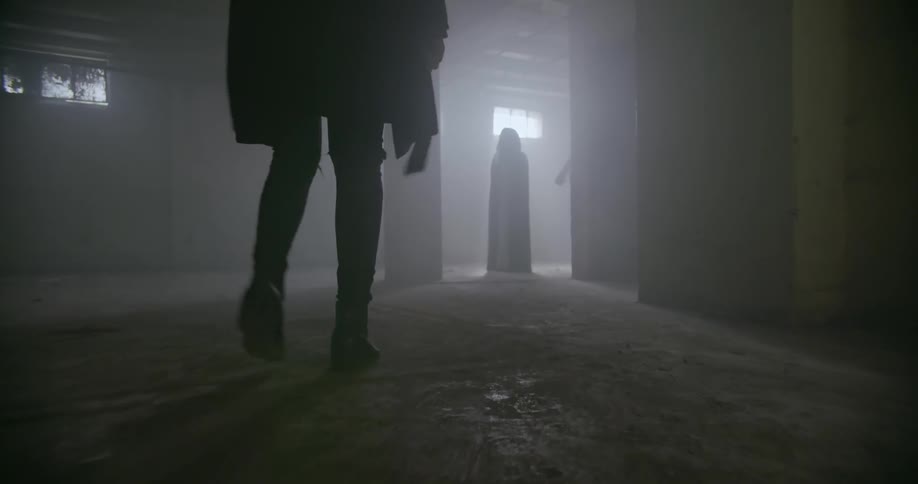 A woman walks towards an ominous figure in a dim room