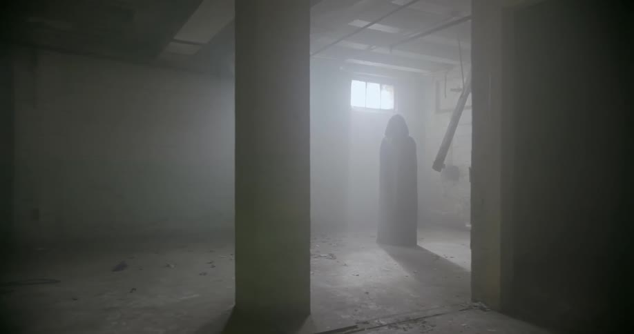 A cloaked woman stands in an abandoned building
