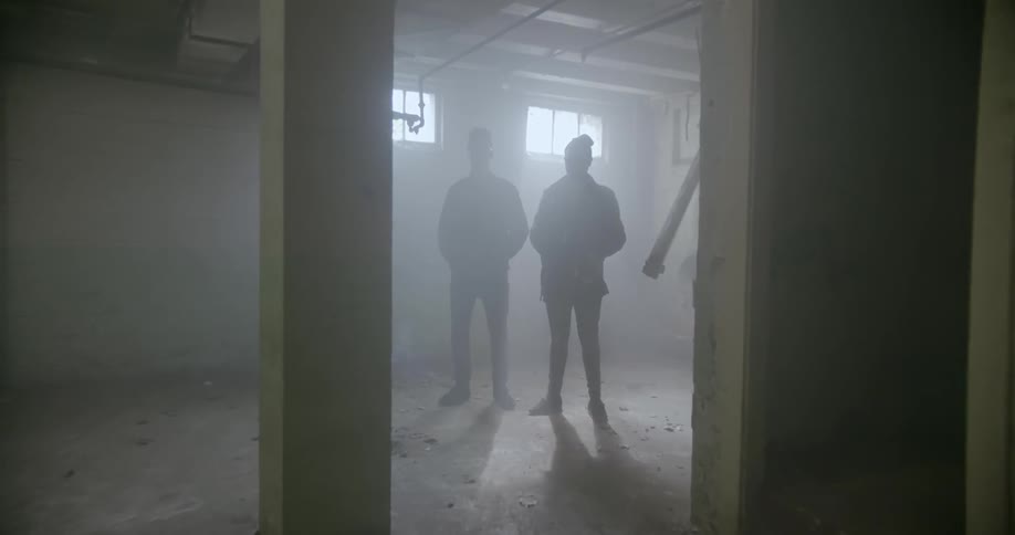 Two people stand together in the basement by the windows