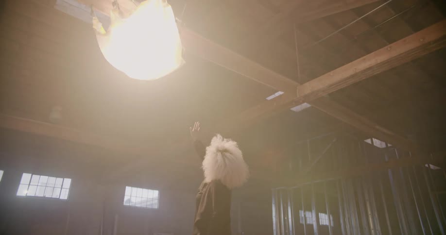 A woman looks up at a flickering light in a warehouse building