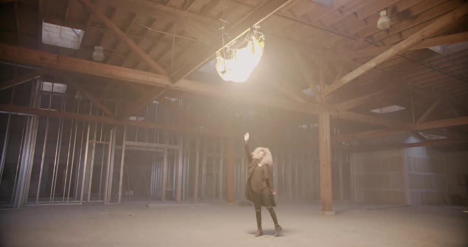 Woman stands beneath a glowing object hanging from a ceiling