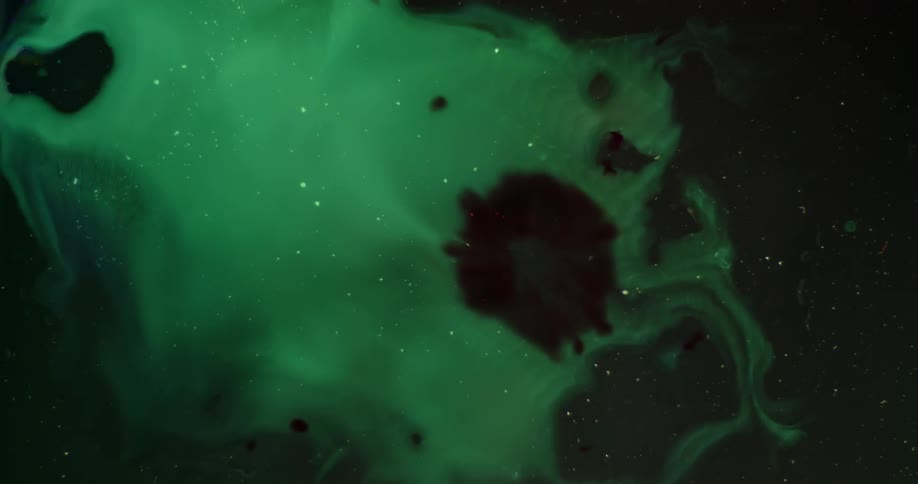 A splattering of dark dye diffuses in a green solution