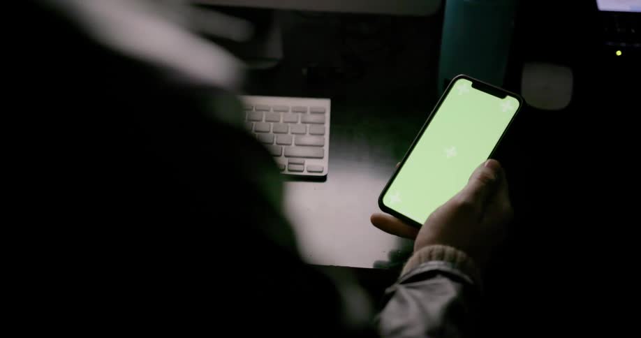 A man holds a smartphone next to a keyboard on a desk