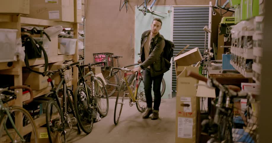 Man walks into bike shop and turns the light on and lays bike on wall
