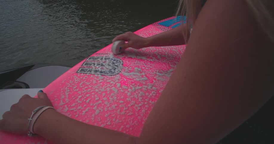 A woman rubs a bright pink wakeboard