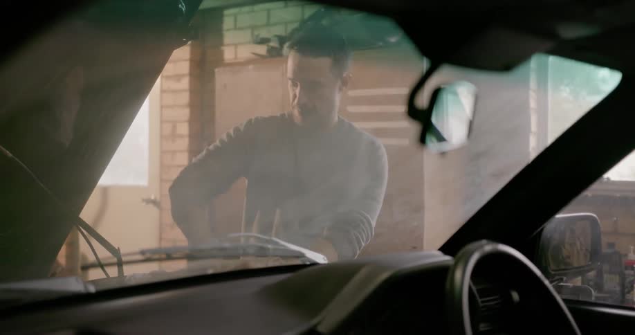 A man is working on a car in a garage during the day