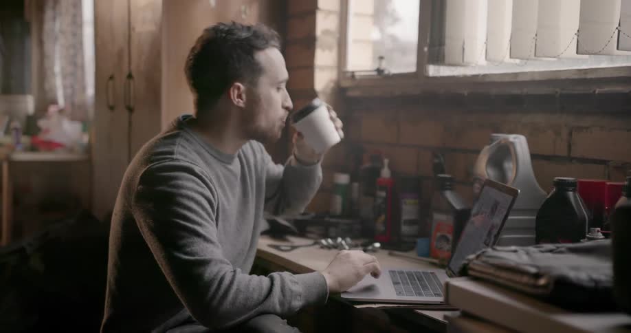 A man sips a coffee as he studies his laptop