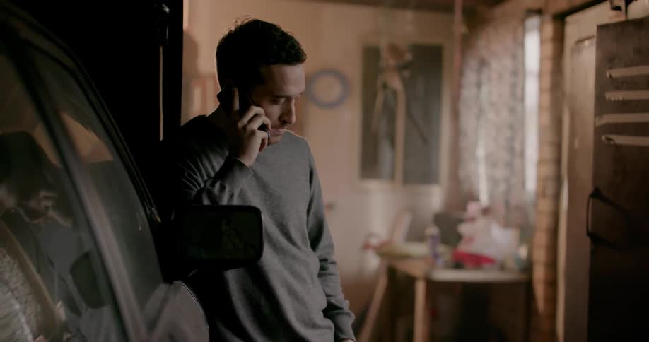 A man is talking on a phone leaning on a car