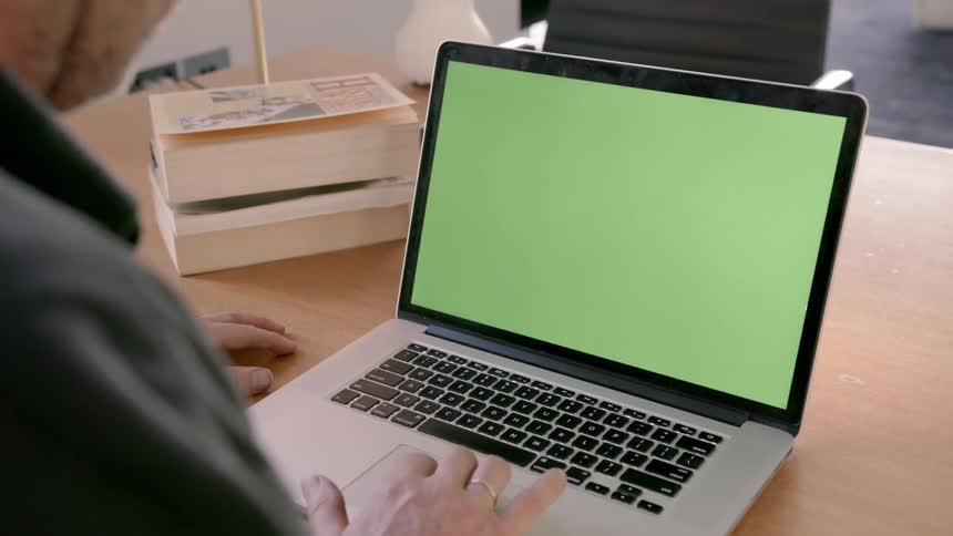 A man uses a laptop with a green screen