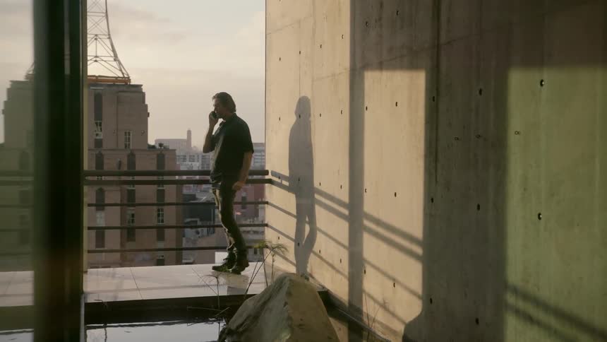 Man stands outside on a balcony talking on a phone