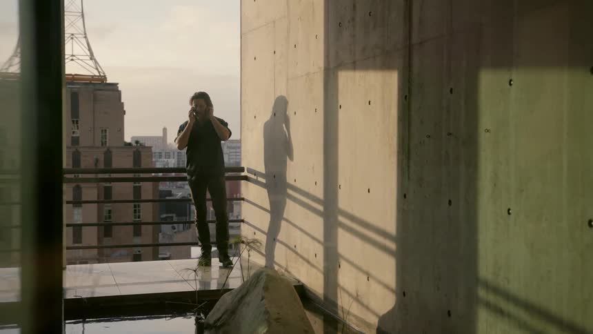 A man is standing on a balcony talking to someone on the phone