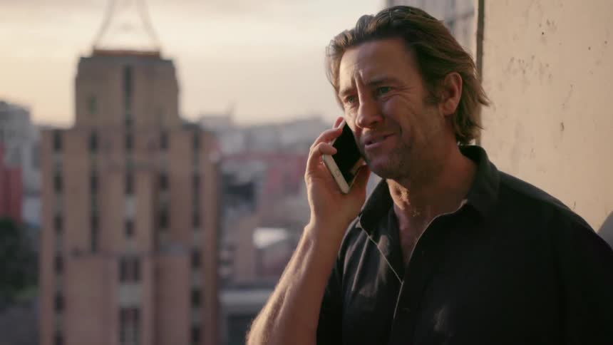 A man laughs as he talks on his phone outside