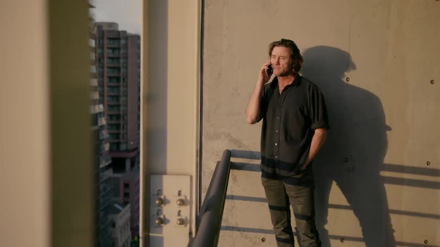A man talks on his phone near the railing of his building