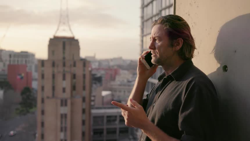 A man talks on his phone by the ledge of a building