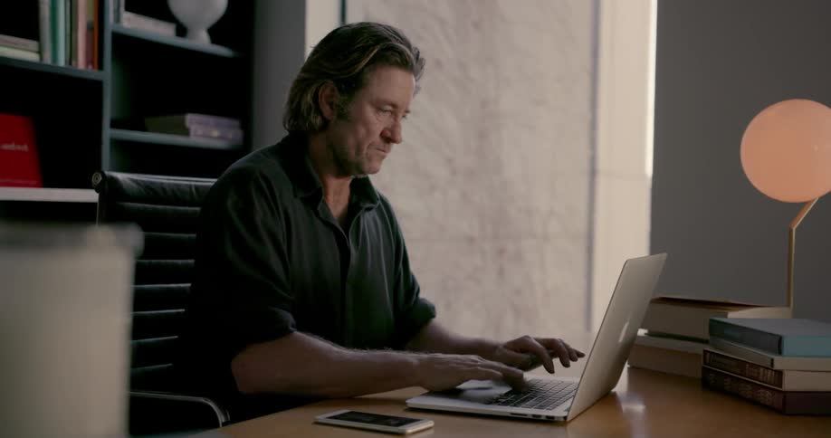 Man sits at a table typing on a laptop