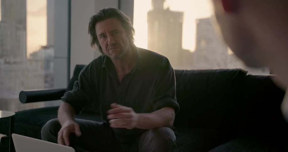 Two men are sitting on couches in an office talking at dusk