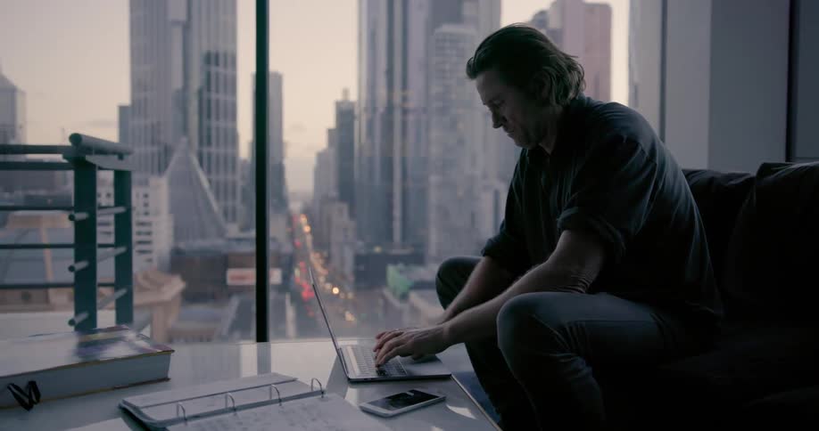 A man is sitting in a dark room using his laptop