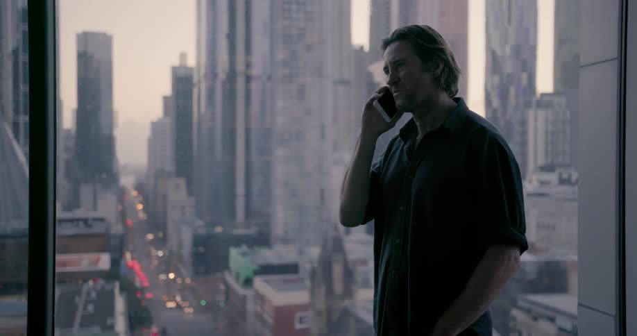 Man talks on phone while standing near a window