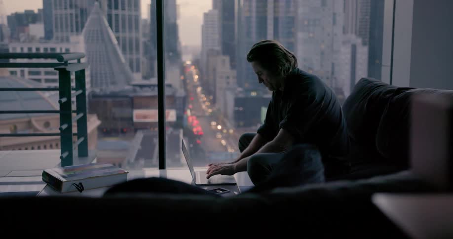 A man is typing on his laptop in the dark living room