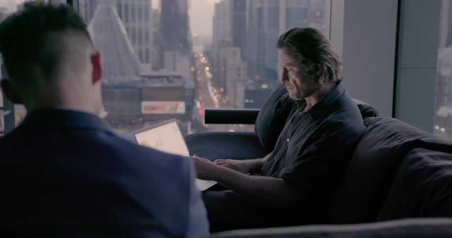 Two men are sitting in an high rise office discussing business at dusk