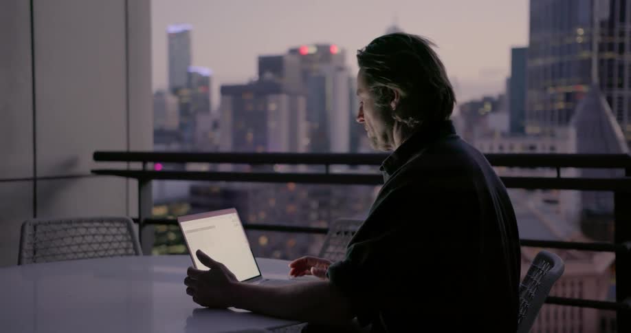 Man works on laptop on city balcony