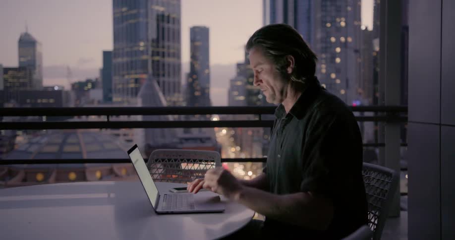 Man looks out window as he types on his laptop