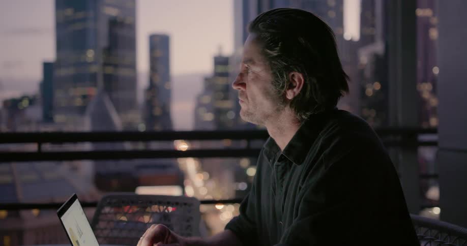 A man sits on a balcony with a laptop