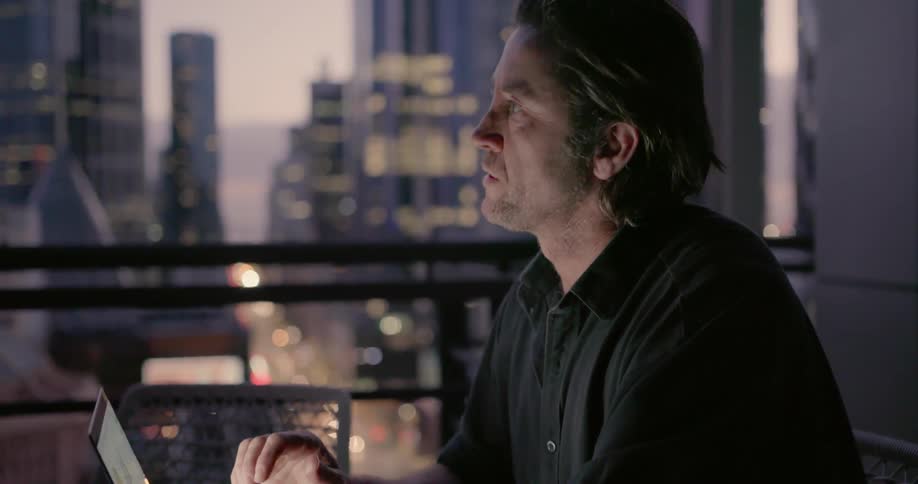 A man sitting at a table on a balcony is working on a laptop