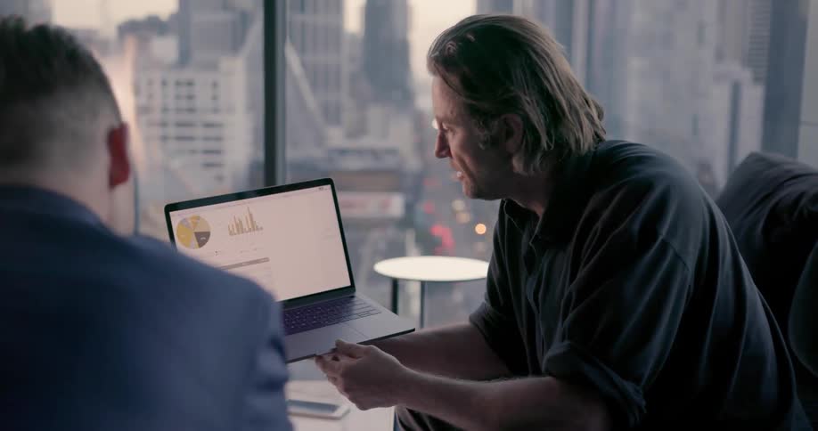 A man smiles and talks as he shows someone diagrams on his laptop