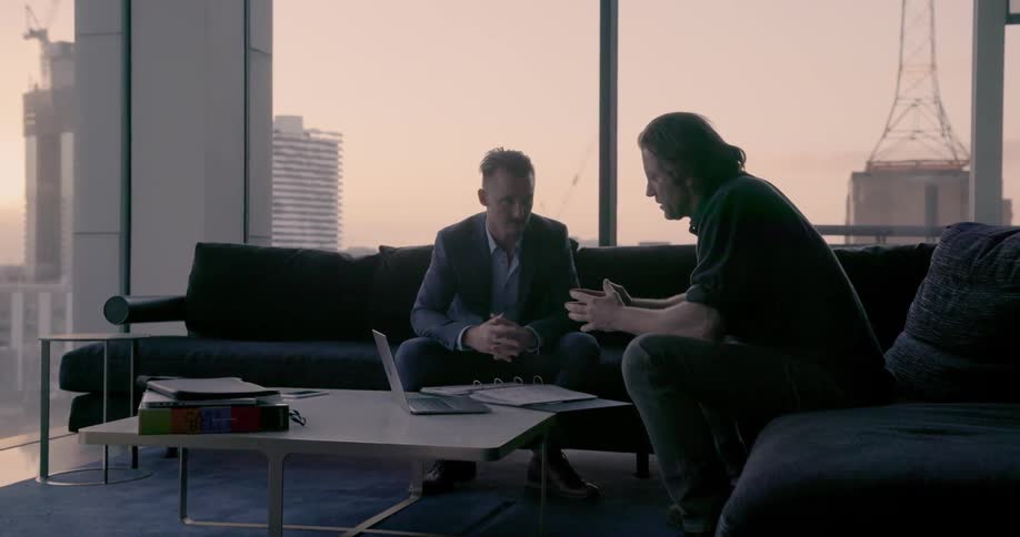 Two men sitting on the couch look at a laptop together