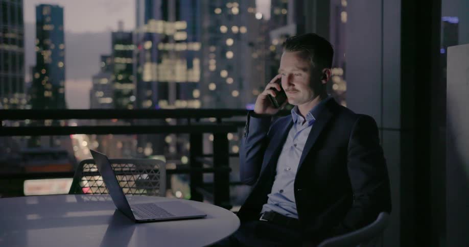 A man smiles as he talks on his phone and uses a laptop