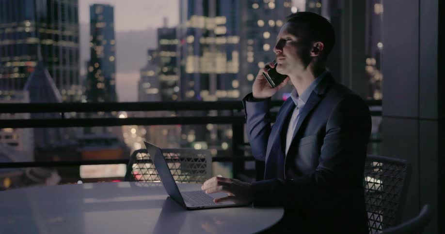 A man sits talking on his phone and using his laptop
