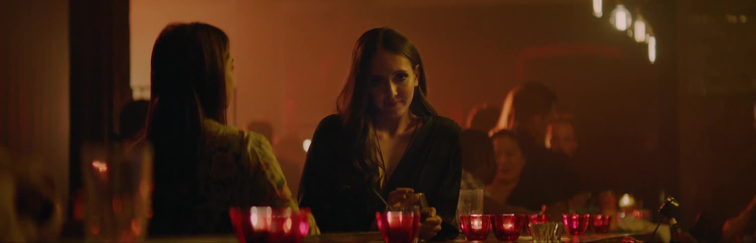 A woman is sitting at a bar with a friend and smiles