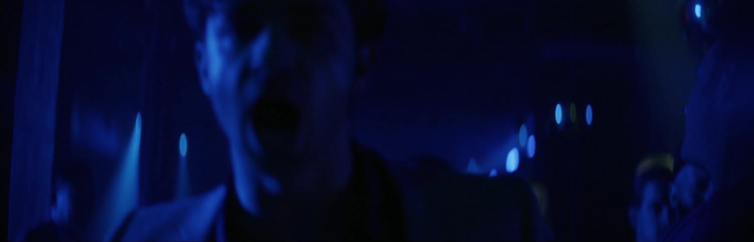 Man yelling and walking forward in a crowded club with lights flashing all around