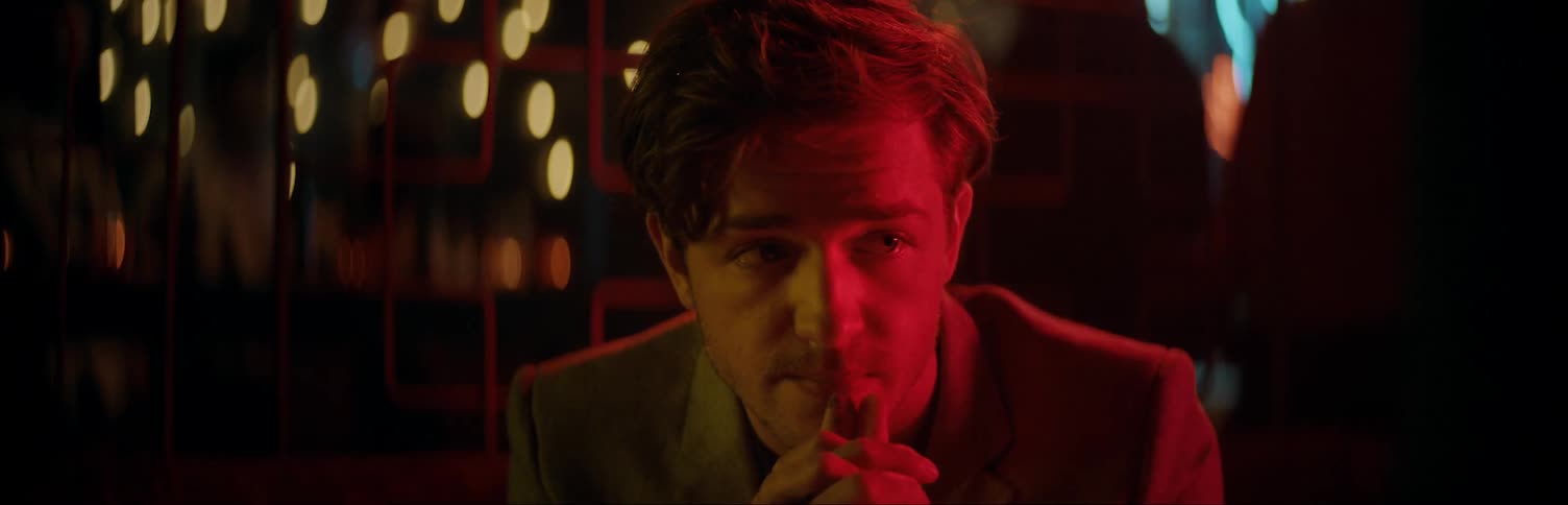 A man sitting in a club at night is glancing around himself