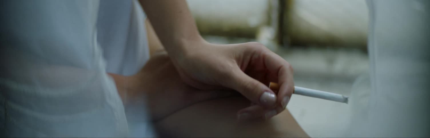 A woman is sitting in a window having a smoke during the day