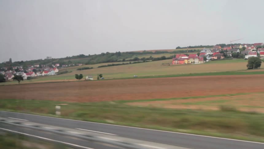 Vehicles on a highway are passing by a rural community on a cloudy day