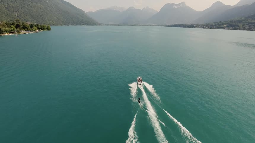 Person wakeboarding on boat in water surrounded by mountains