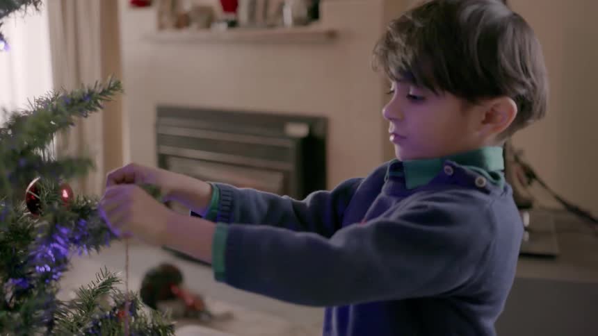 A young boy places ornaments on a christmas tree