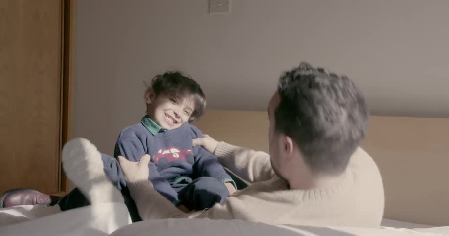 A boy and a man are wrestling on a bed during the day