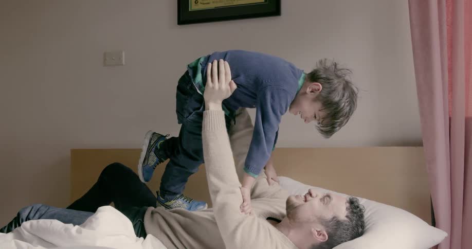 A man is holding a boy in the air as they play on a bed during the day