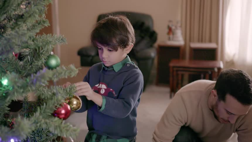 A young boy places ornaments on a christmas tree