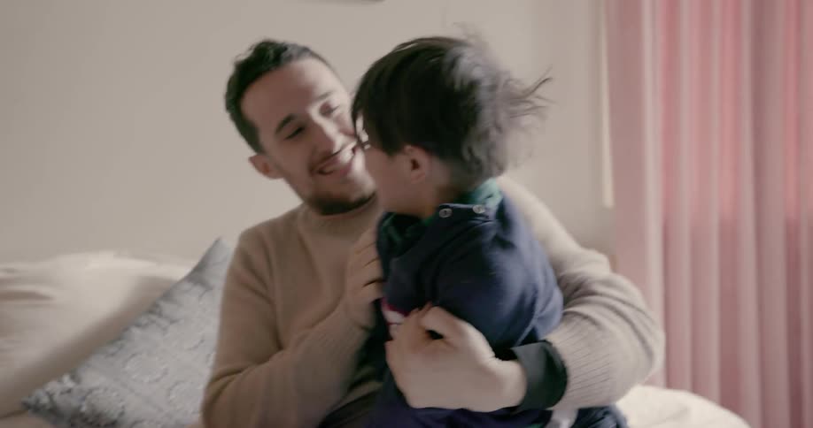 A man and little boy are wrestling on a bed during the day