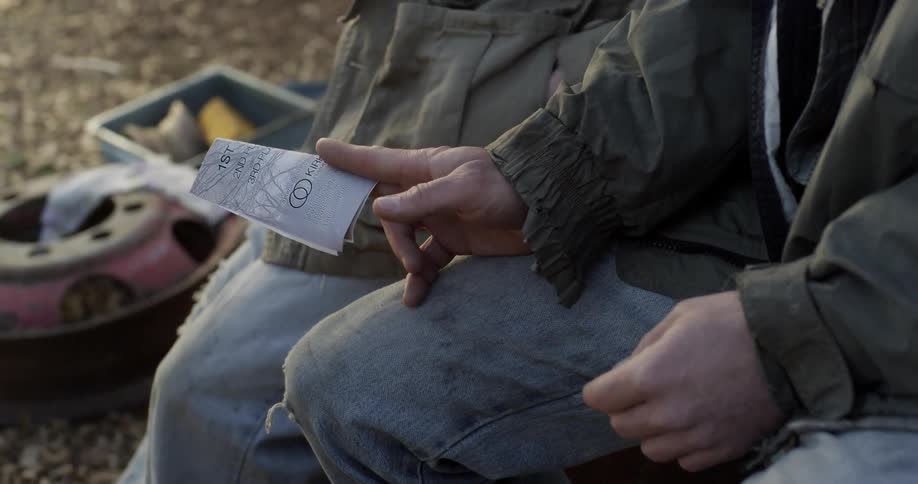 Two people are sitting outside and one hands the other a note