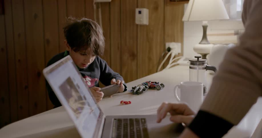 Man looks at a laptop while boy plays on phone