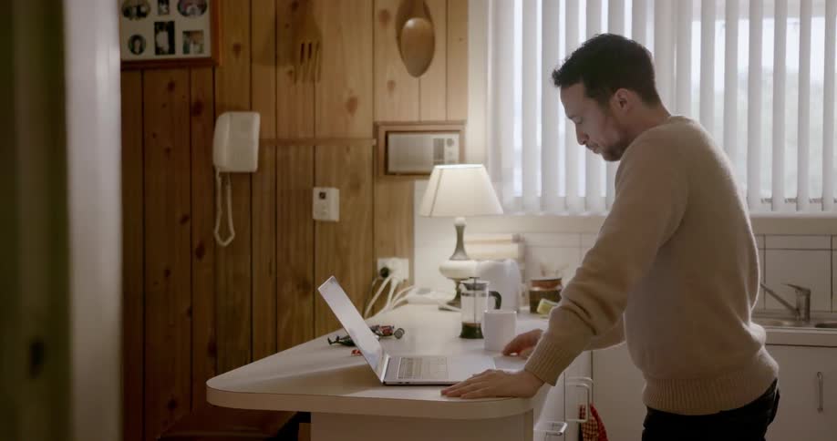 A man drinks from his coffee as he looks at his laptop