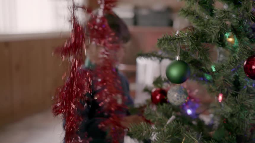 Young boy helps decorate a christmas tree with tinsel