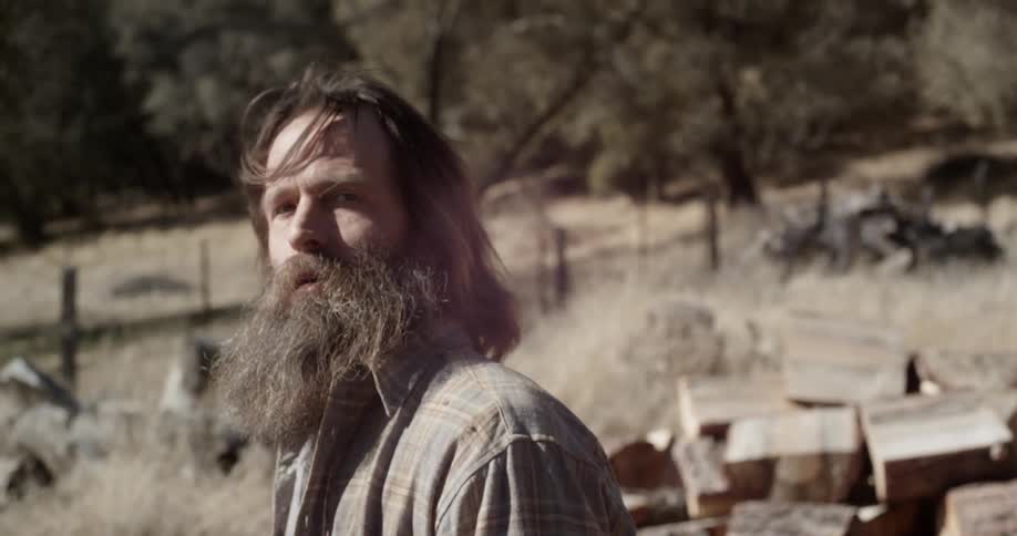 A bearded man sets up a piece of wood to be chopped