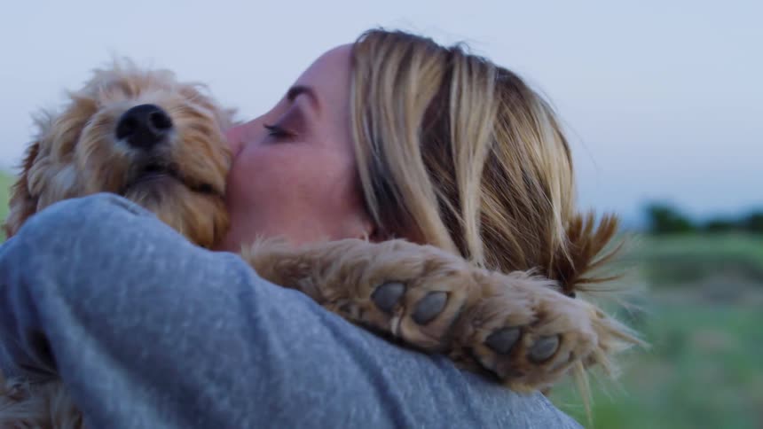 A woman is holding and kissing a fluffy dog
