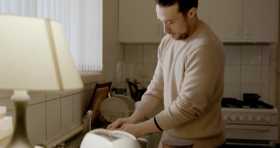 Man washes dishes at kitchen sink